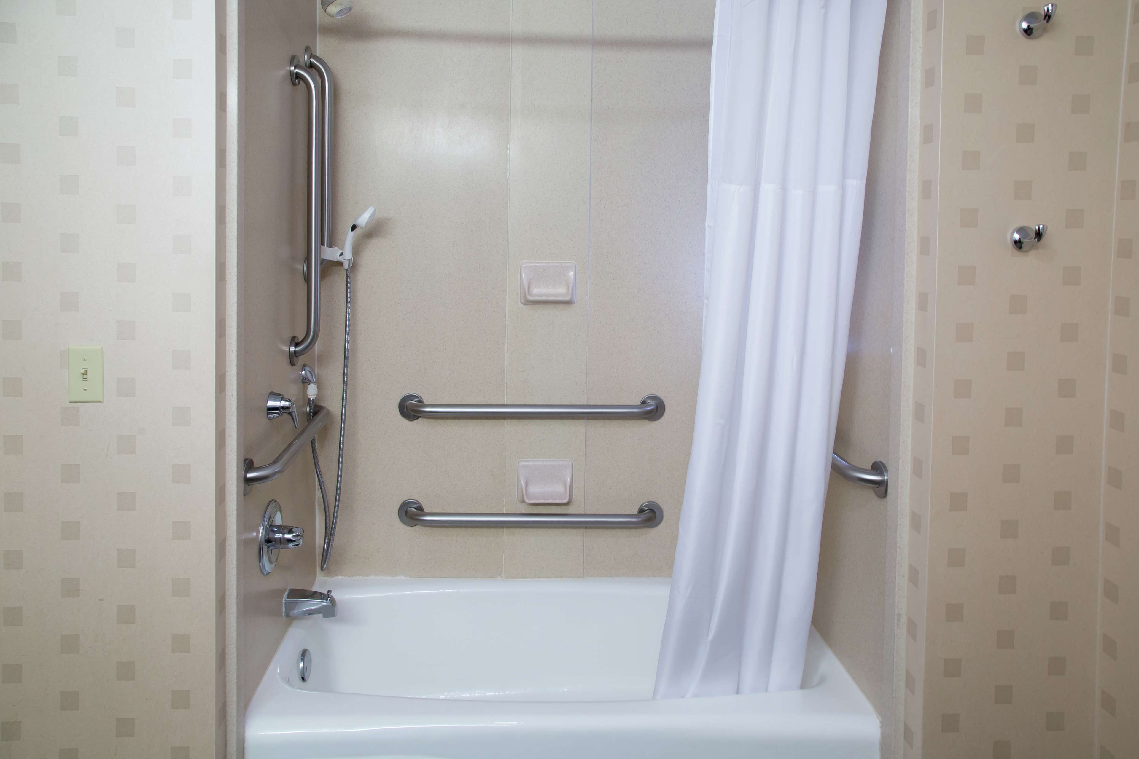 Un baño con bañera, barras de apoyo y cortina de ducha.