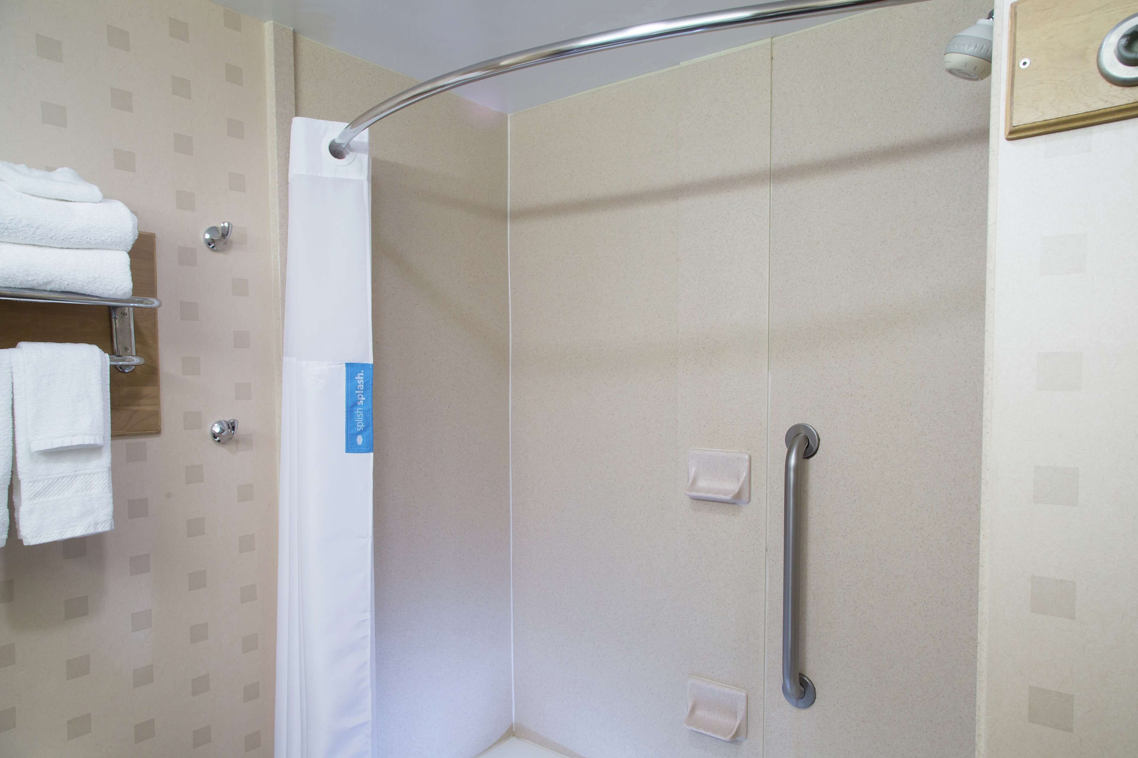 A shower area with a white curtain, a grab bar, and a towel rack with folded towels.