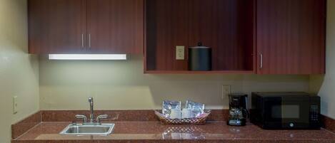 A kitchen with wooden cabinets, a stainless steel sink, a coffee maker, and a microwave.
