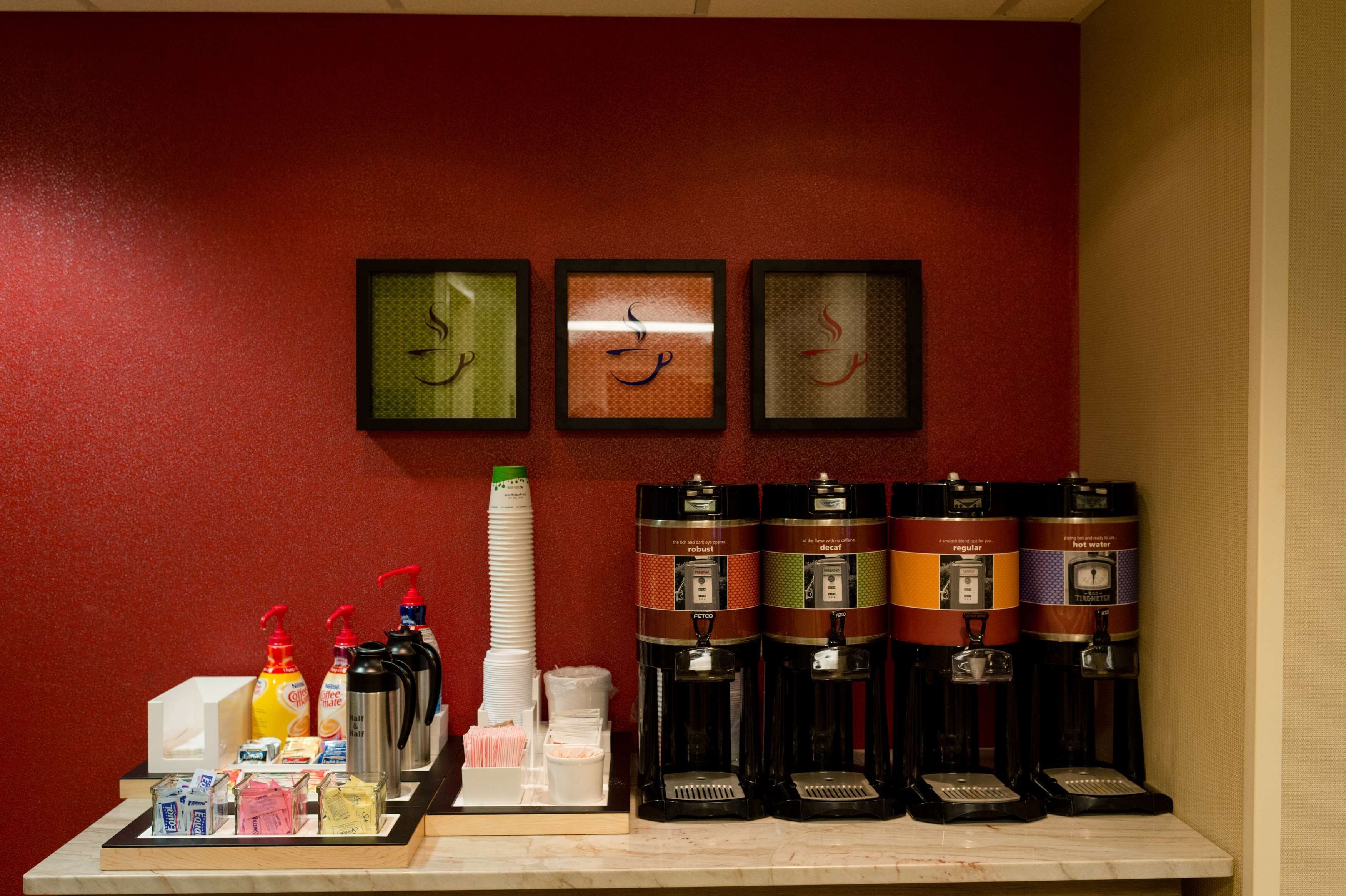 A coffee station with multiple dispensers and a variety of condiments and snacks.