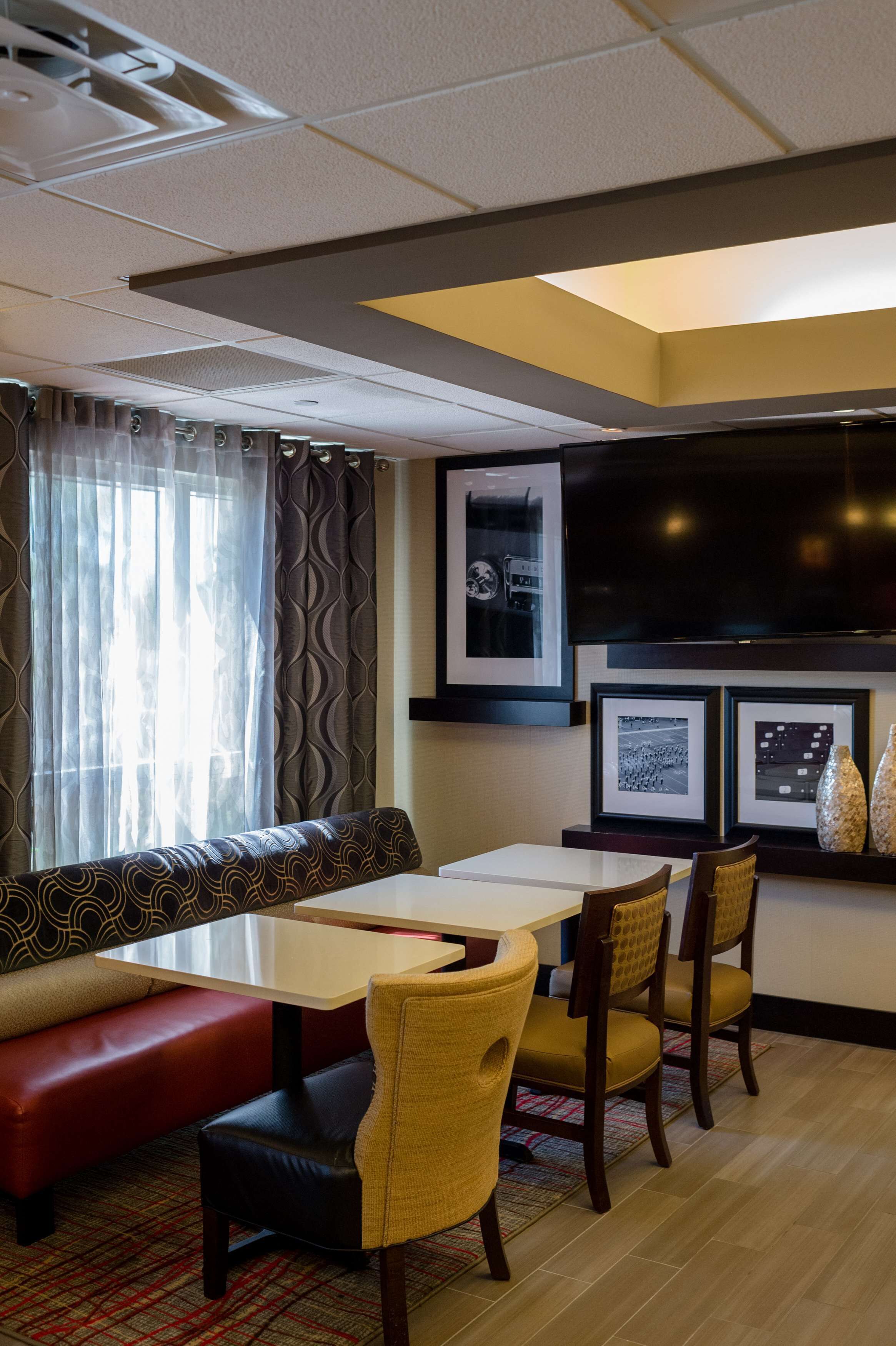 A hotel room with a sofa, dining table, chairs, a flat-screen TV, and framed pictures on the wall.