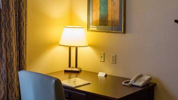 Habitación de hotel con escritorio, silla, lámpara, teléfono y un cuadro en la pared.