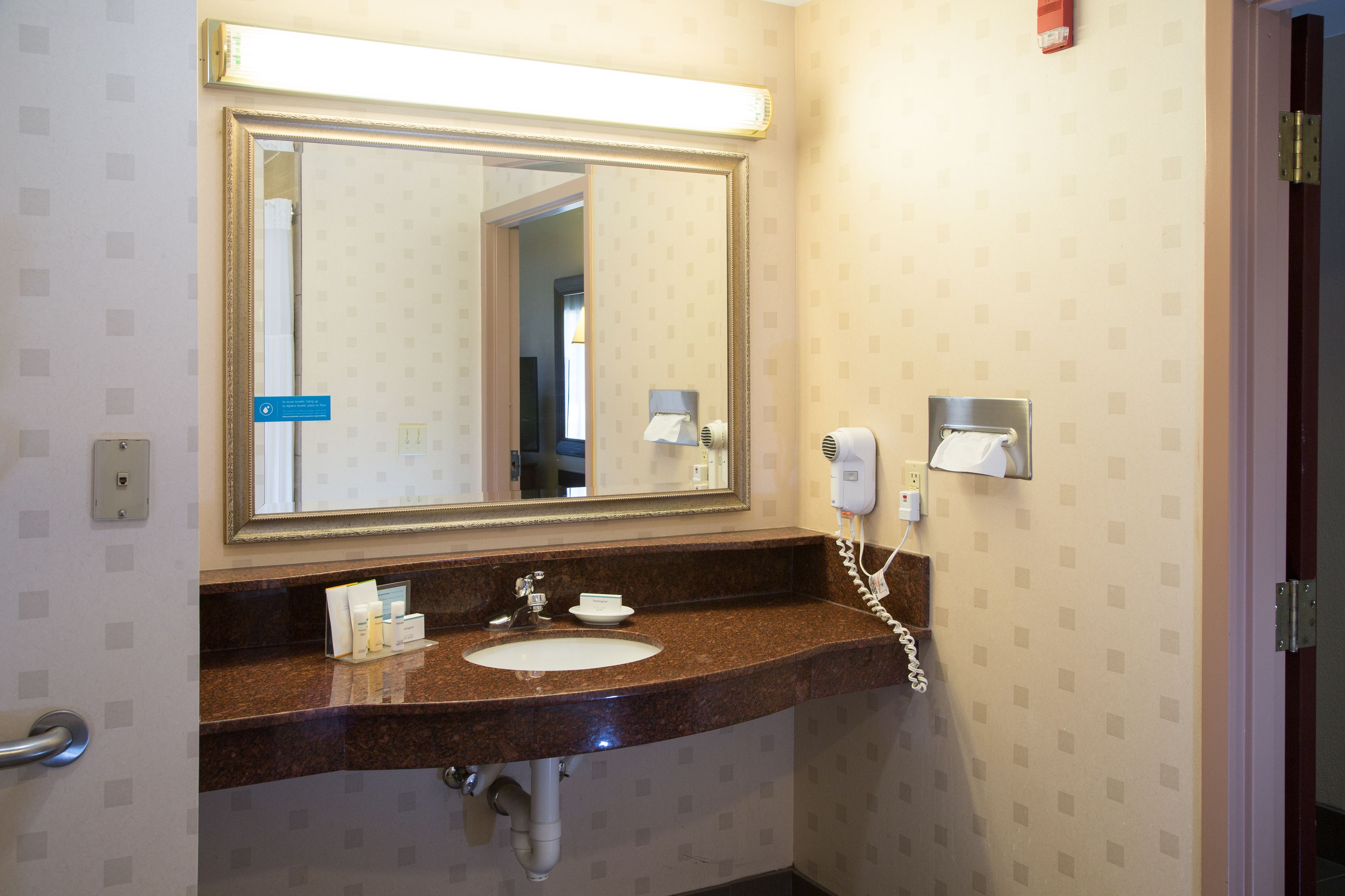 A bathroom with a sink, mirror, and towel dispenser.