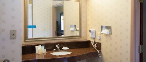 A bathroom with a sink, mirror, and towel dispenser.