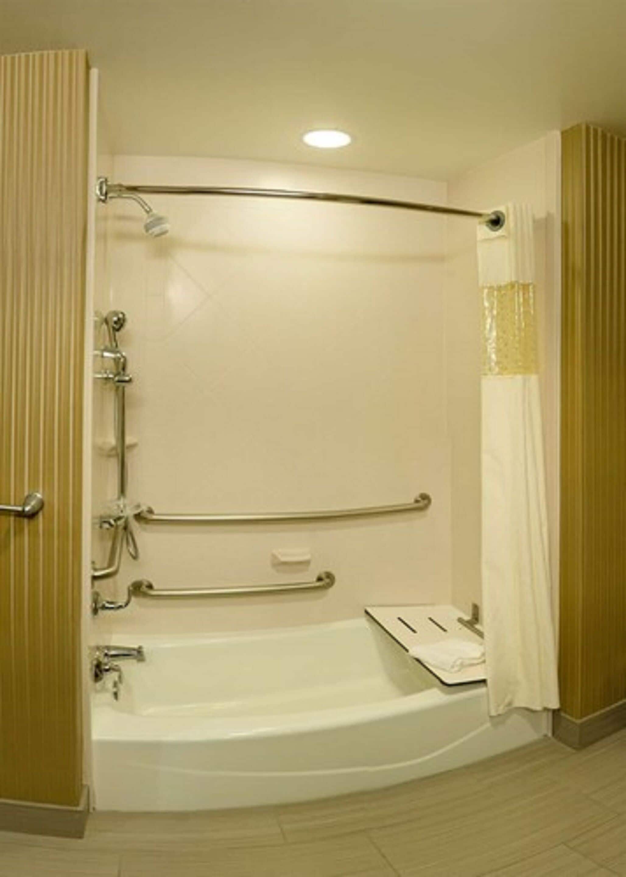 Une salle de bain d’hôtel standard, équipée d’une baignoire, d’une douche et de barres d’appui.
