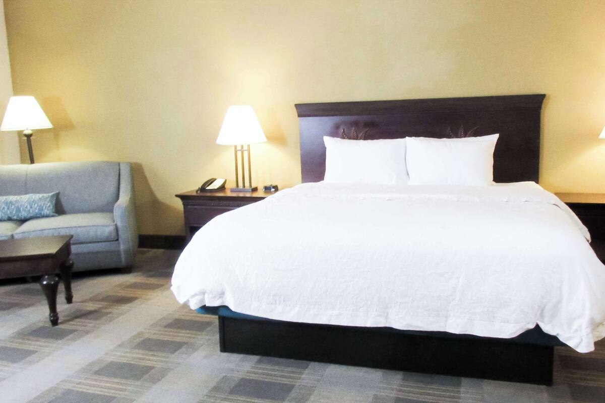 A hotel room with a large bed, two bedside tables with lamps, a sofa with a cushion, and a telephone on one of the tables.