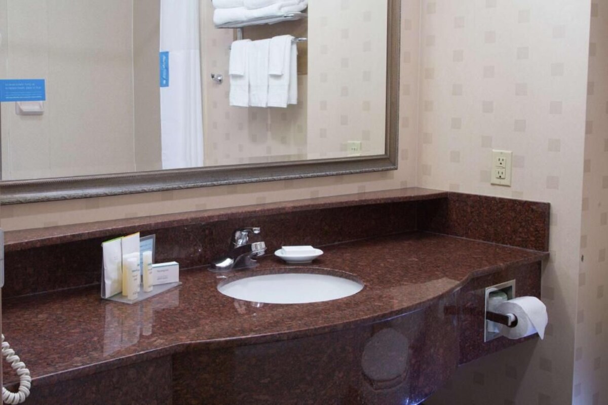 A bathroom with a marble sink, a mirror, a towel rack with folded towels, a soap dispenser, and a toilet paper holder.