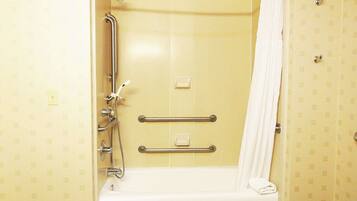 A bathroom with a bathtub, a shower, and a handrail.