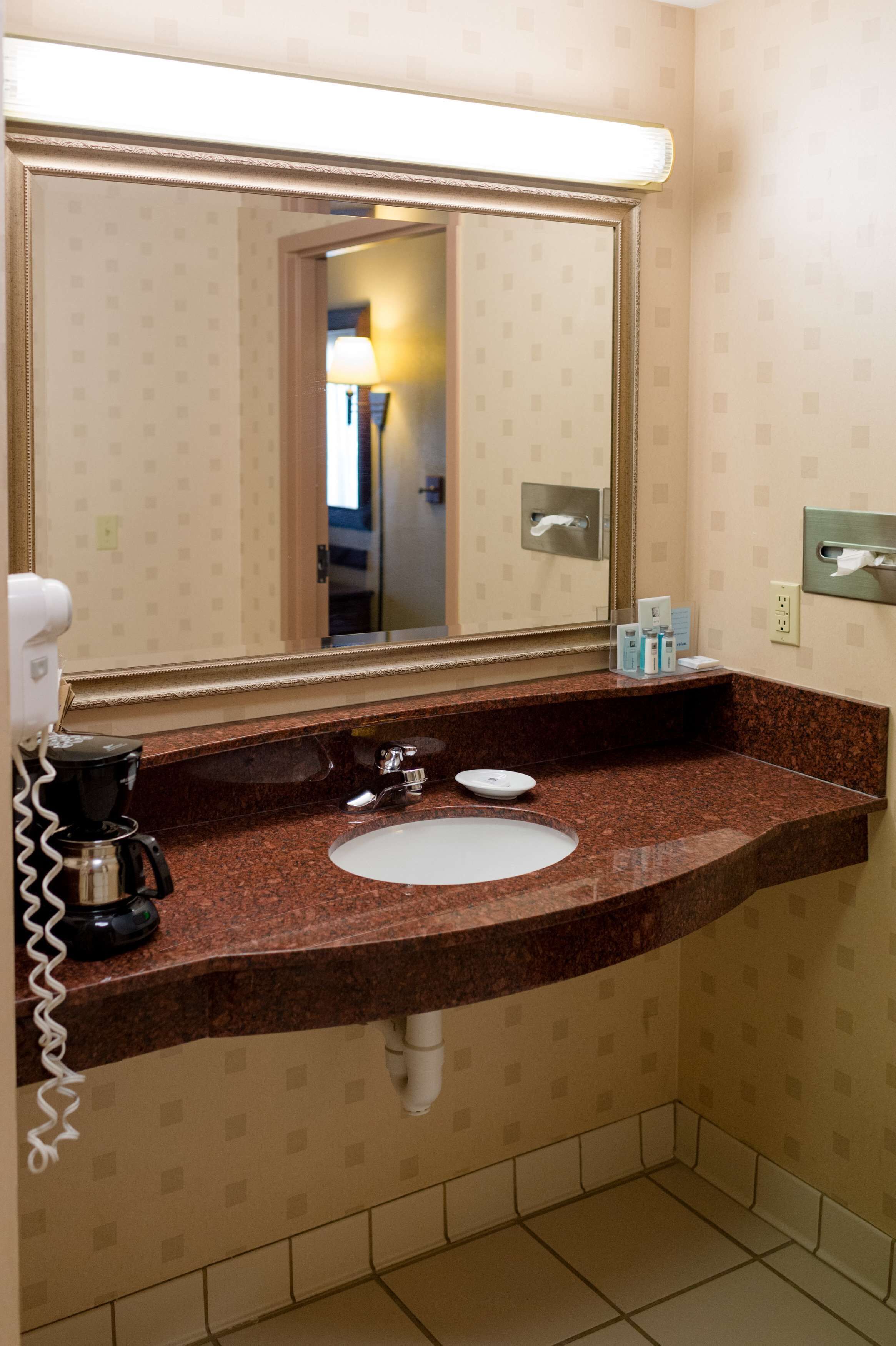 Een badkamer met een marmeren wastafel, een spiegel, een zeepdispenser en een koffiezetapparaat.