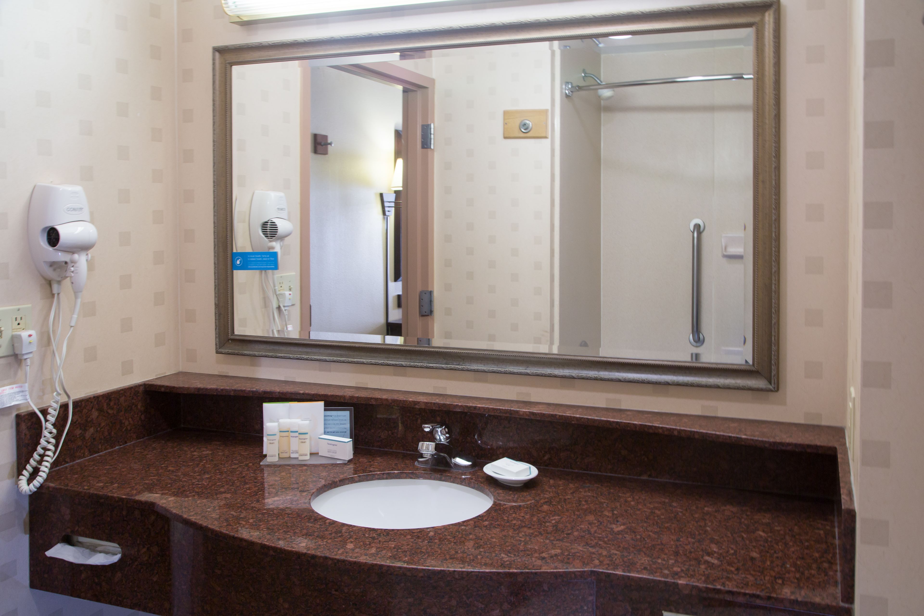Une salle de bain avec un grand miroir, un lavabo, un sèche-cheveux et une douche.