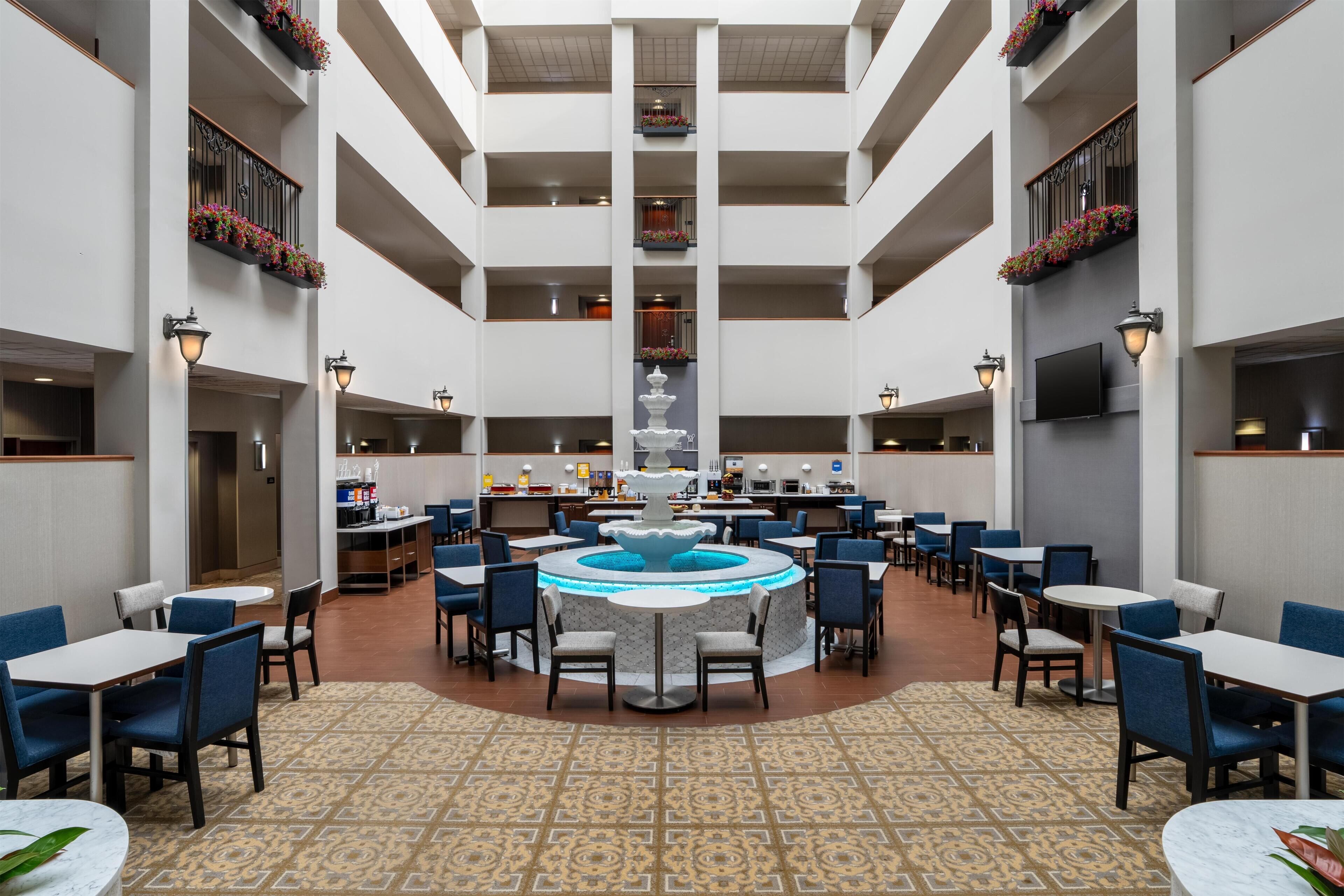 A spacious hotel lobby with multiple dining areas, a central fountain, and balconies with flower boxes.