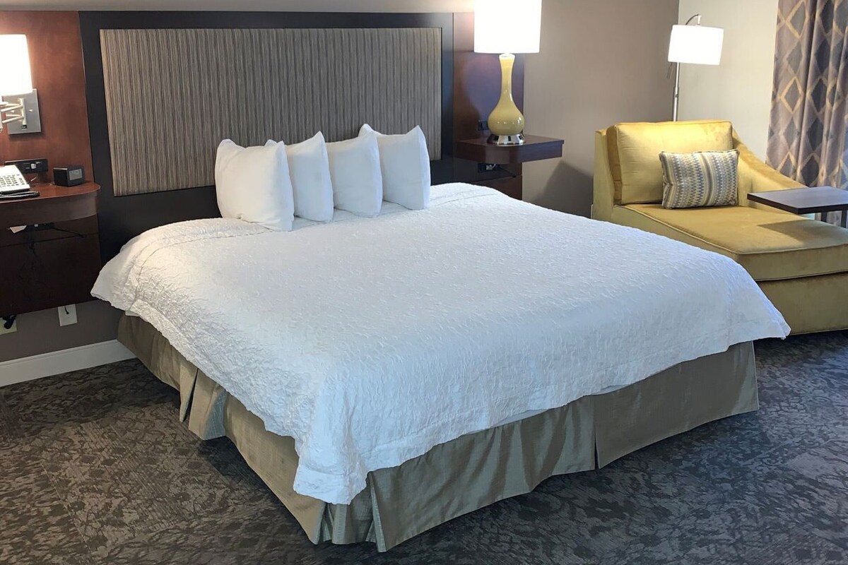 A hotel room with a large bed, a sofa, two bedside tables with lamps, and a headboard.
