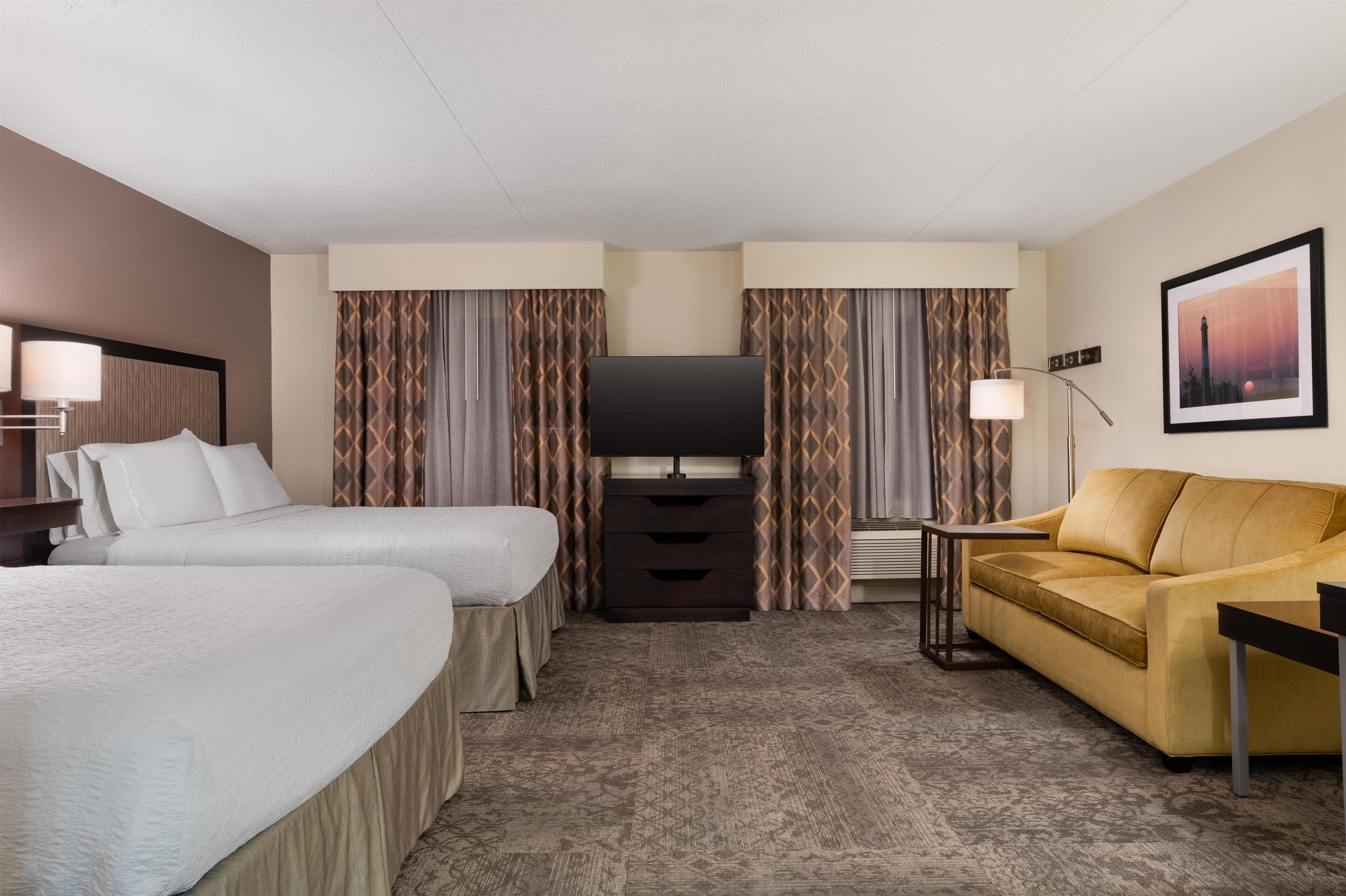Ein Hotelzimmer mit zwei Betten, einem Sofa, einem Fernseher und einer Lampe.