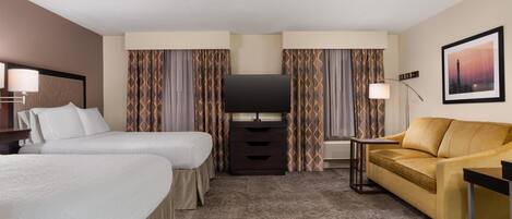 Ein Hotelzimmer mit zwei Betten, einem Sofa, einem Fernseher und einer Lampe.