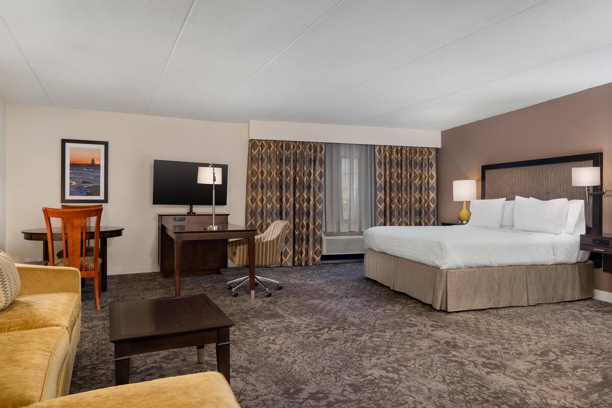 Ett hotellrum med en säng, ett skrivbord med en stol, en tv och ett litet bord.