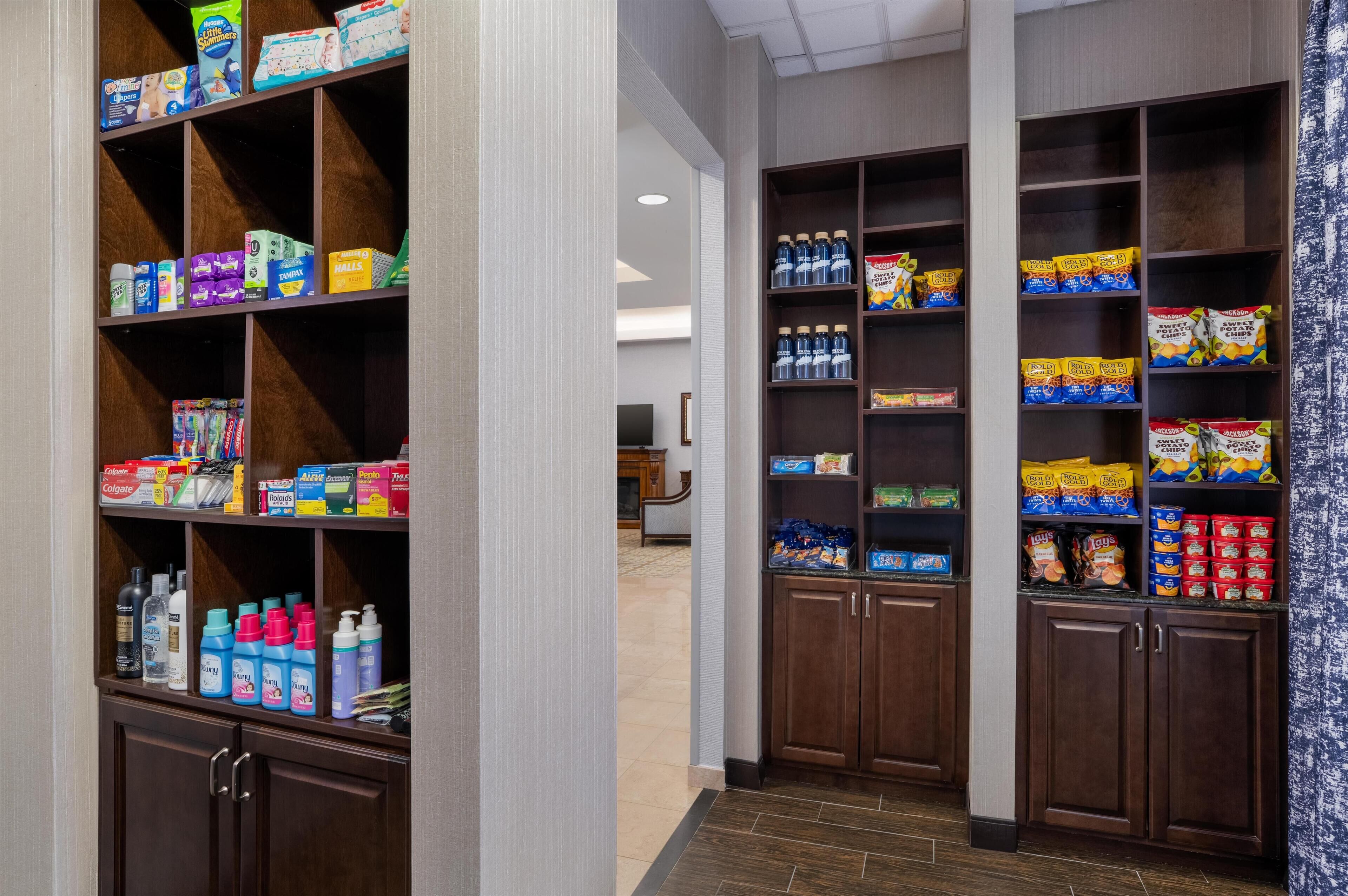 A hotel lobby with a self-service beverage station and a variety of toiletries on shelves.
