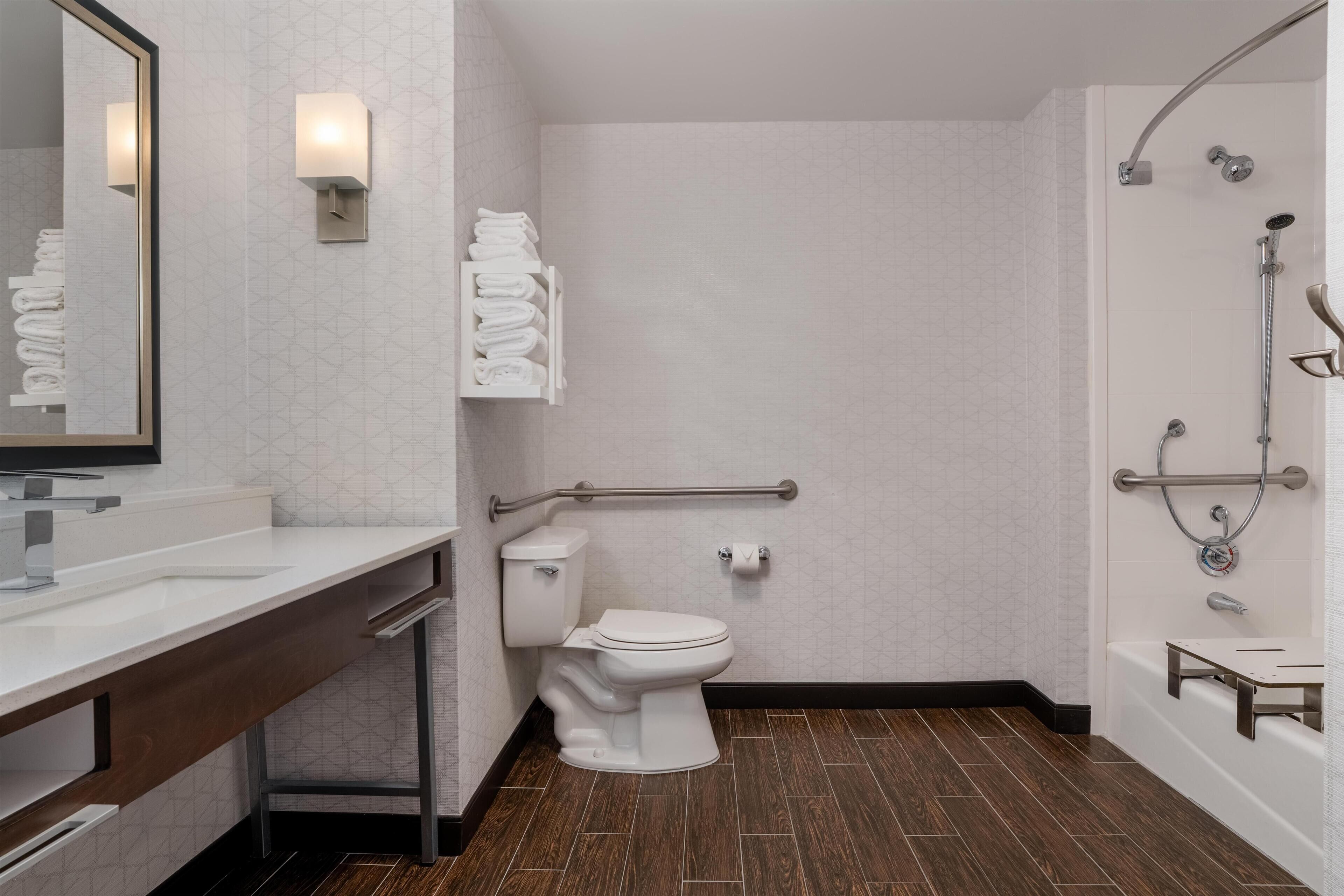 A modern bathroom with a white toilet, a sink with a mirror, and a shower area with a grab bar.