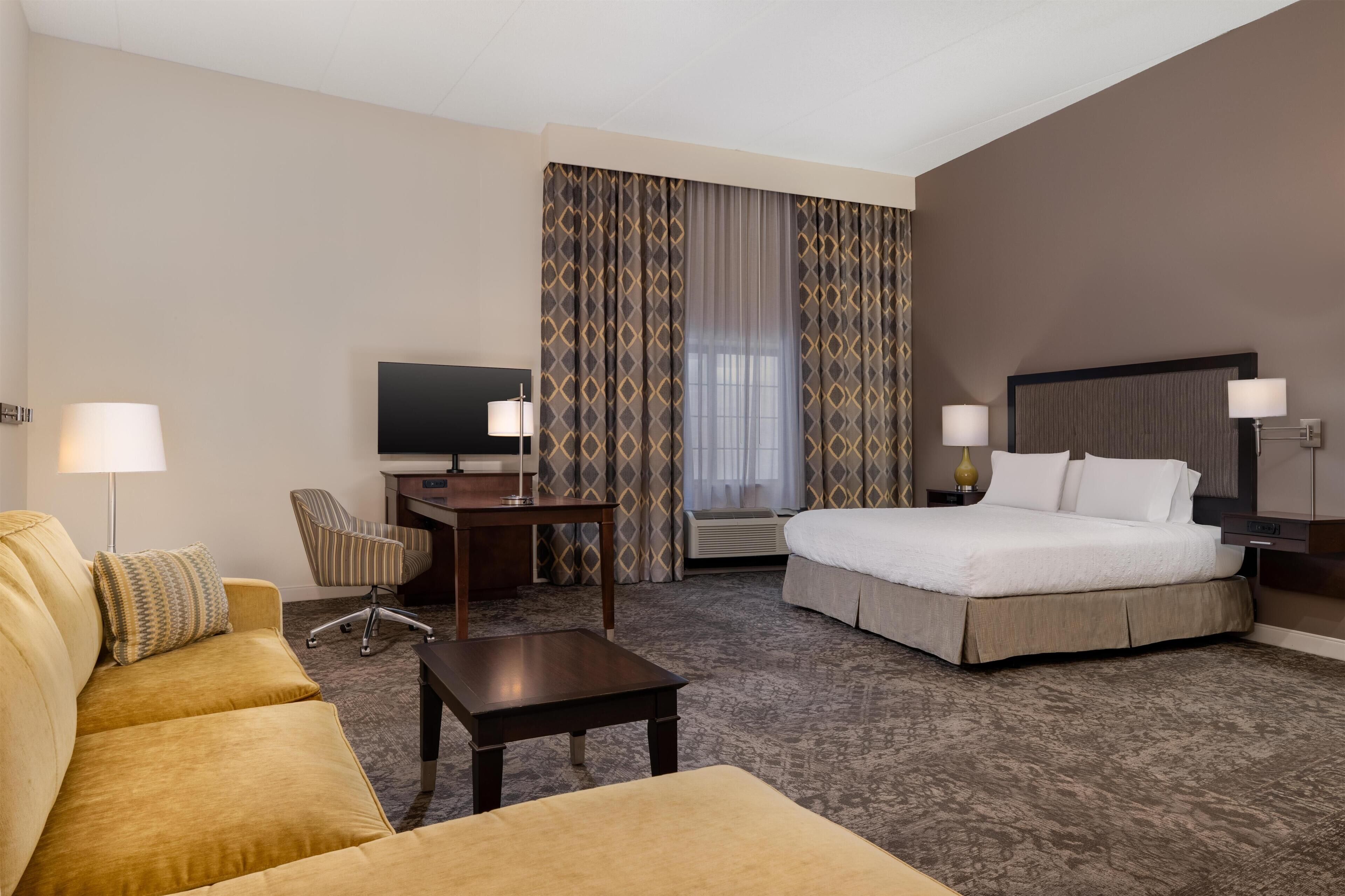 A hotel room with a bed, a desk, a chair, a sofa, and a television.