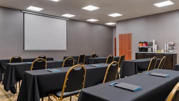 Ein Konferenzraum mit Tischen und Stühlen, einer Projektionsleinwand und einer Kaffeestation.