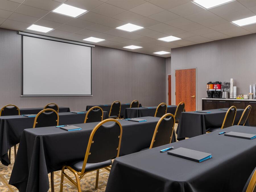 Ein Konferenzraum mit Tischen und Stühlen, einer Projektionsleinwand und einer Kaffeestation.