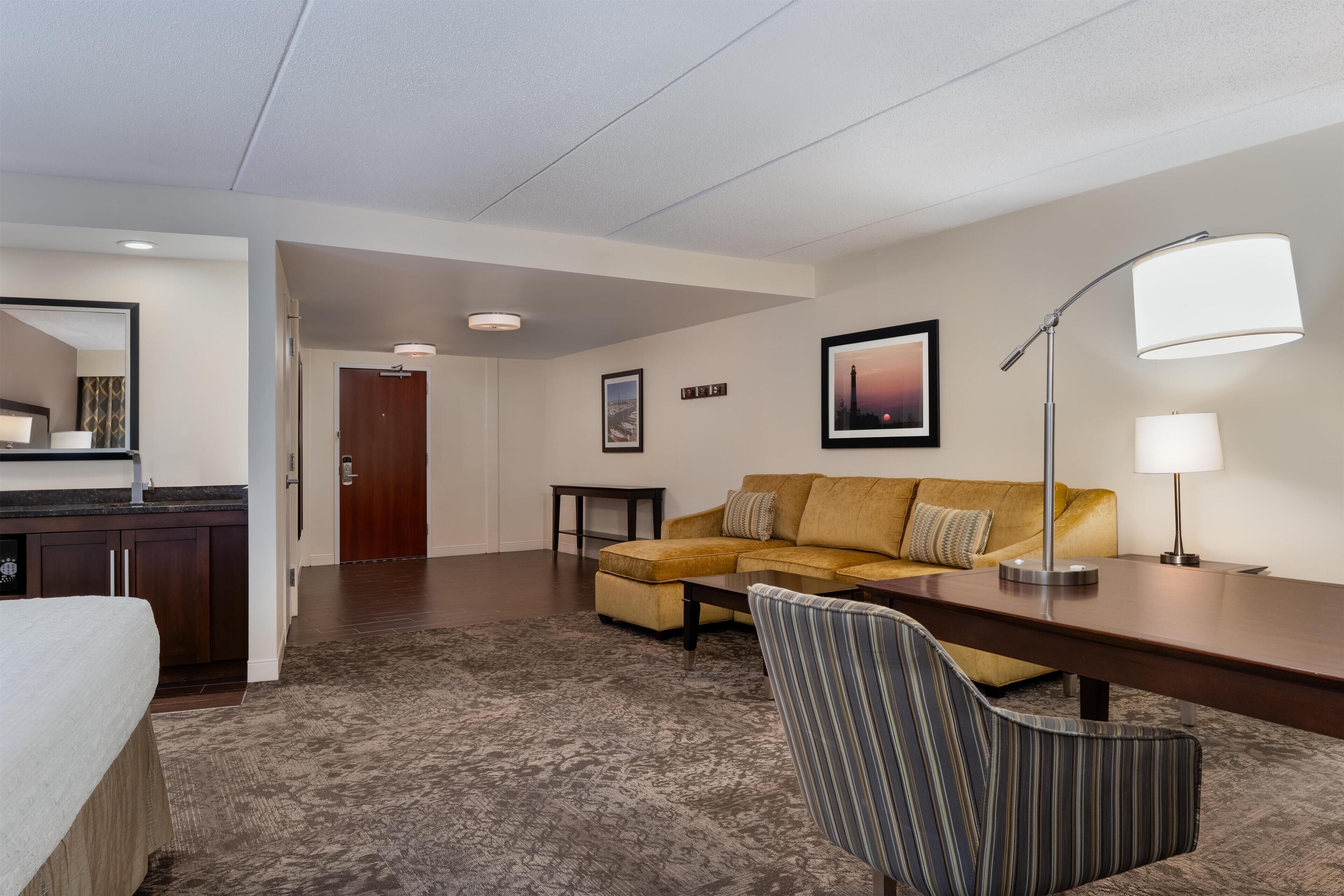 Habitación de hotel con sofá, sillón, mesa de comedor y una zona de cocina con fregadero y armarios.