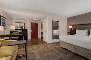 Une chambre d’hôtel avec un grand lit, un bureau avec une chaise, une petite kitchenette et une salle de bain visible à travers une porte ouverte.