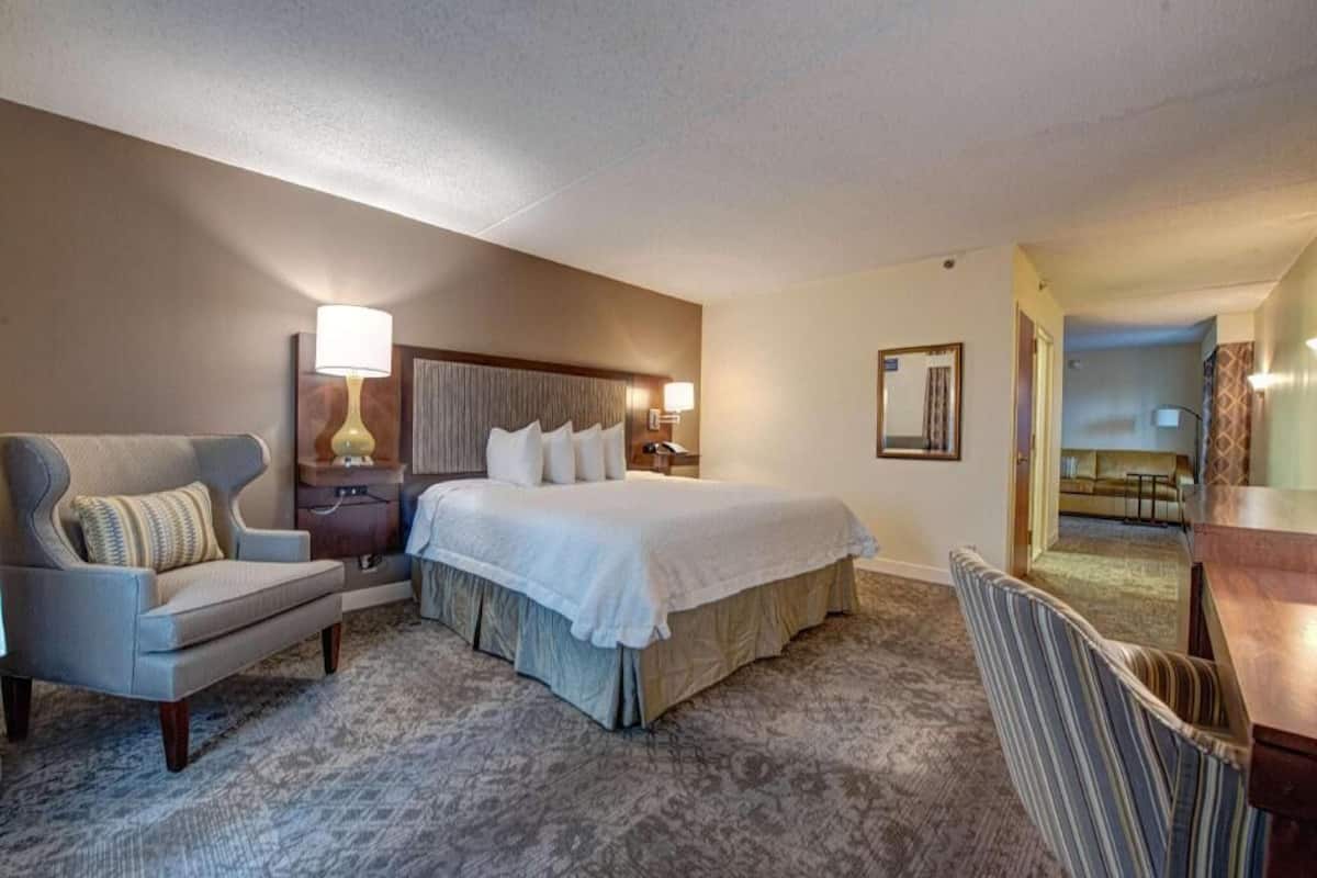 A hotel room with a bed, a chair, a desk, a lamp, and a mirror.