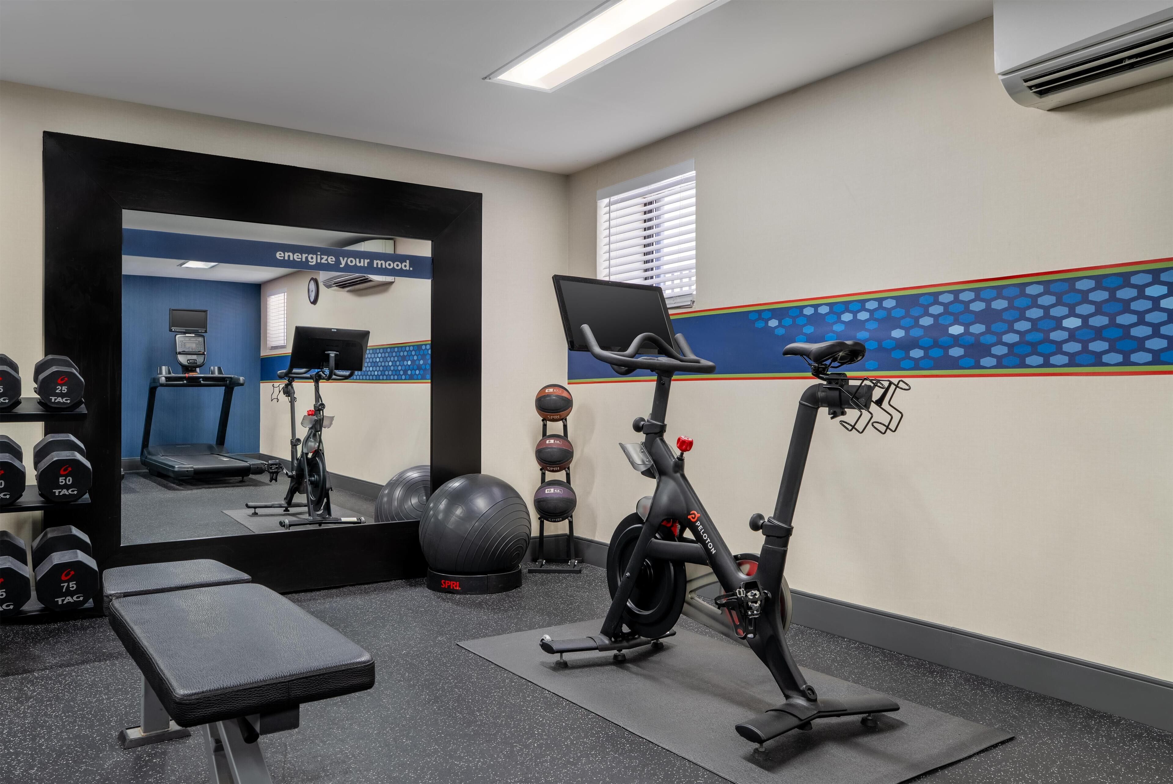 Une salle de sport équipée de matériel d’exercice, d’un tapis de course et d’un miroir.