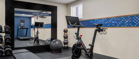 Une salle de sport équipée de matériel d’exercice, d’un tapis de course et d’un miroir.