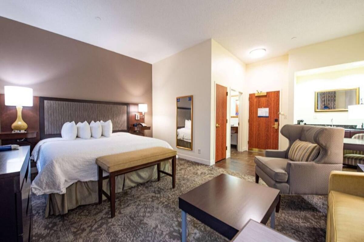 A hotel room with a bed, bedside table, lamp, chair, and a small table.