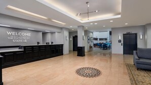 A modern hotel lobby with a reception desk, a welcome sign, a dining area, and a seating area. - Hampton Inn & Suites Rockville Centre (Rockville Centre)