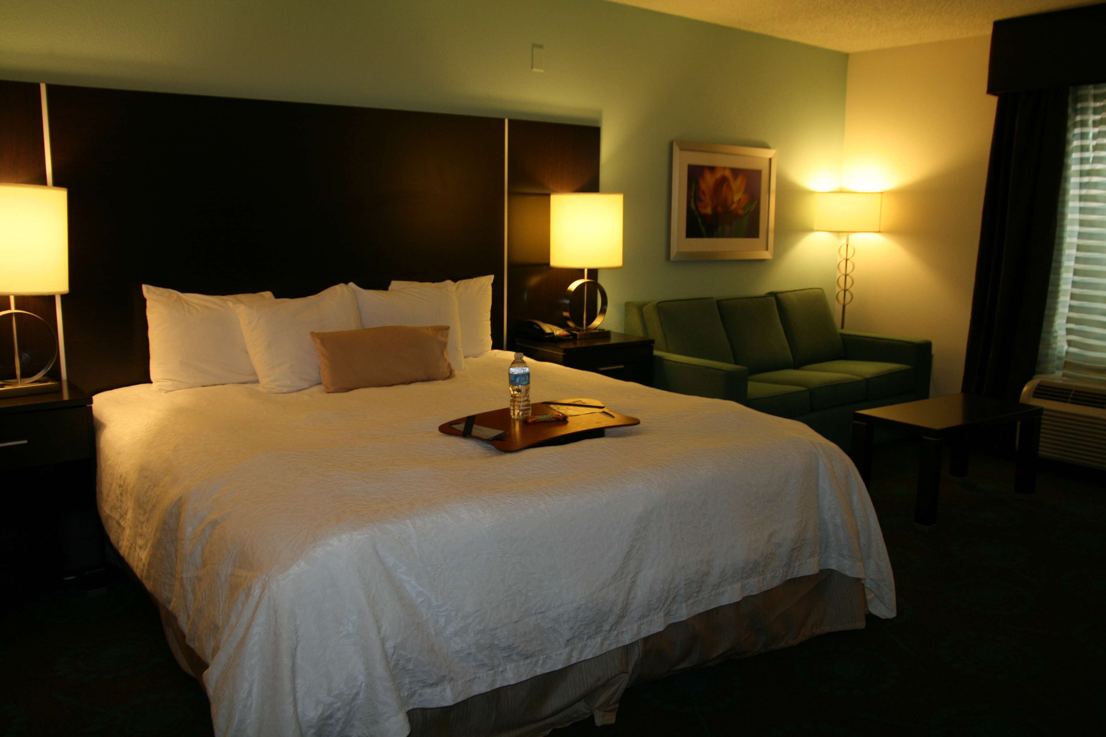 Una habitación de hotel con una cama grande, dos lámparas de noche, un sillón verde y una mesita.
