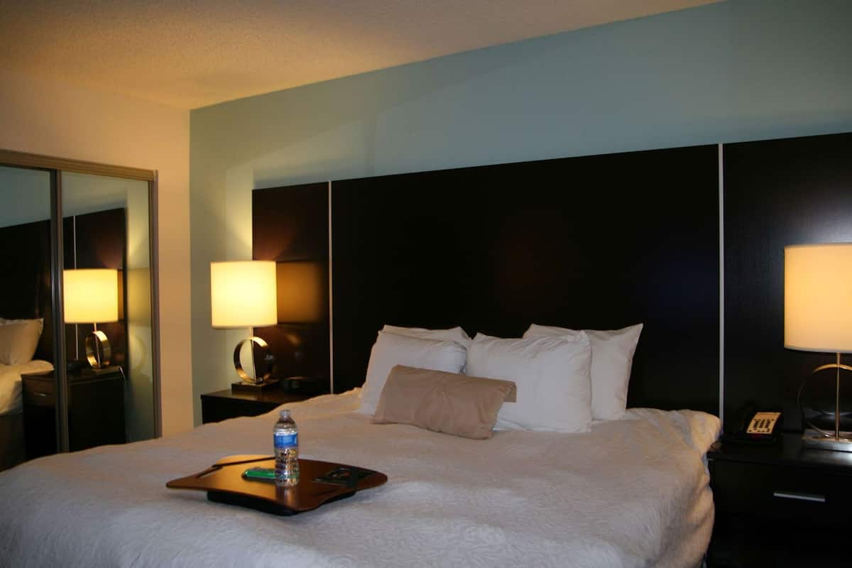 Una habitación de hotel con una cama grande, lámparas de noche, una mesita de noche y un espejo.