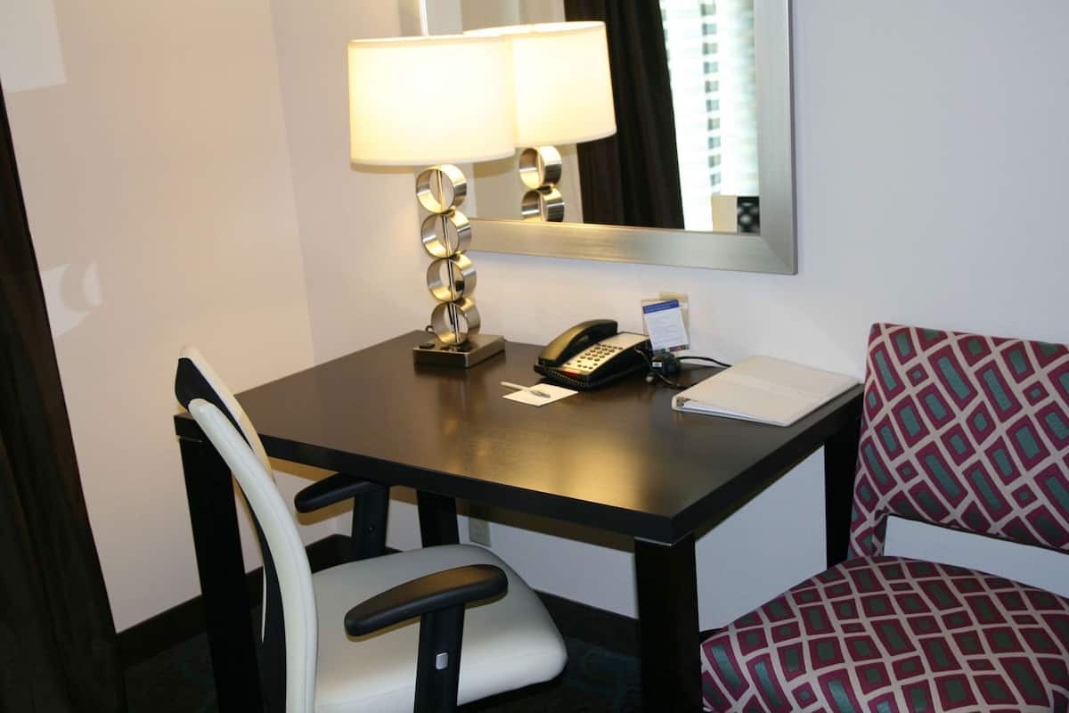 Una habitación de hotel con escritorio, teléfono, lámpara, silla y libreta.