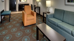 A hotel room with a sofa, armchair, and a small table. There is a mirror on the wall and a picture frame. The room has a carpet with a circular pattern. - Hampton Inn Shreveport Airport (Shreveport)