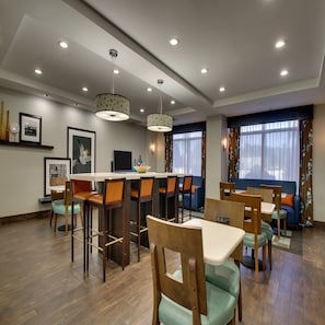 Un espace de restauration moderne avec des tables et des chaises en bois, un éclairage encastré au plafond et de grandes fenêtres agrémentées de rideaux.