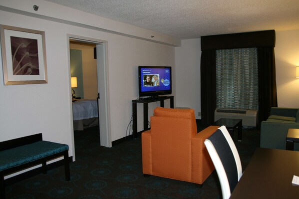 Una habitación de hotel con televisión, cama, sofá, sillón y mesa.
