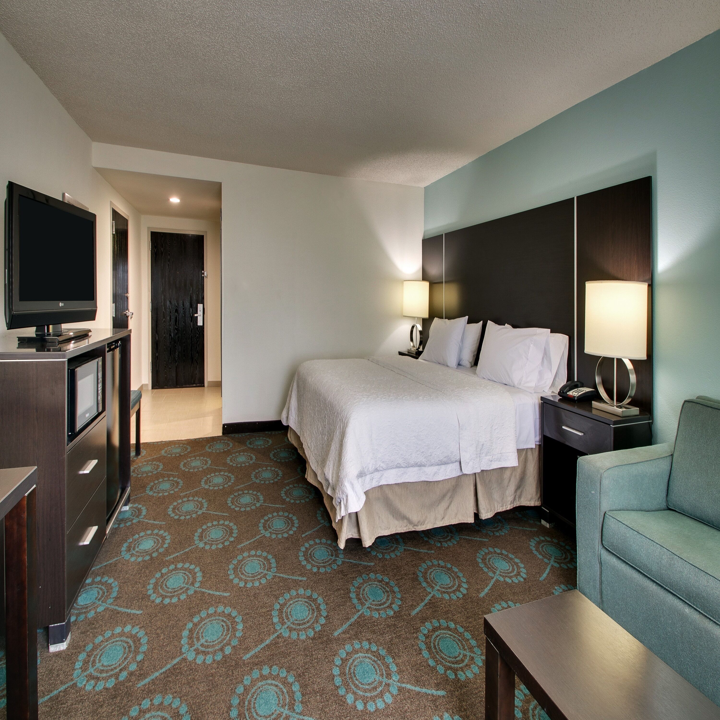 A hotel room with a bed, bedside lamps, a TV, a desk, and a chair.