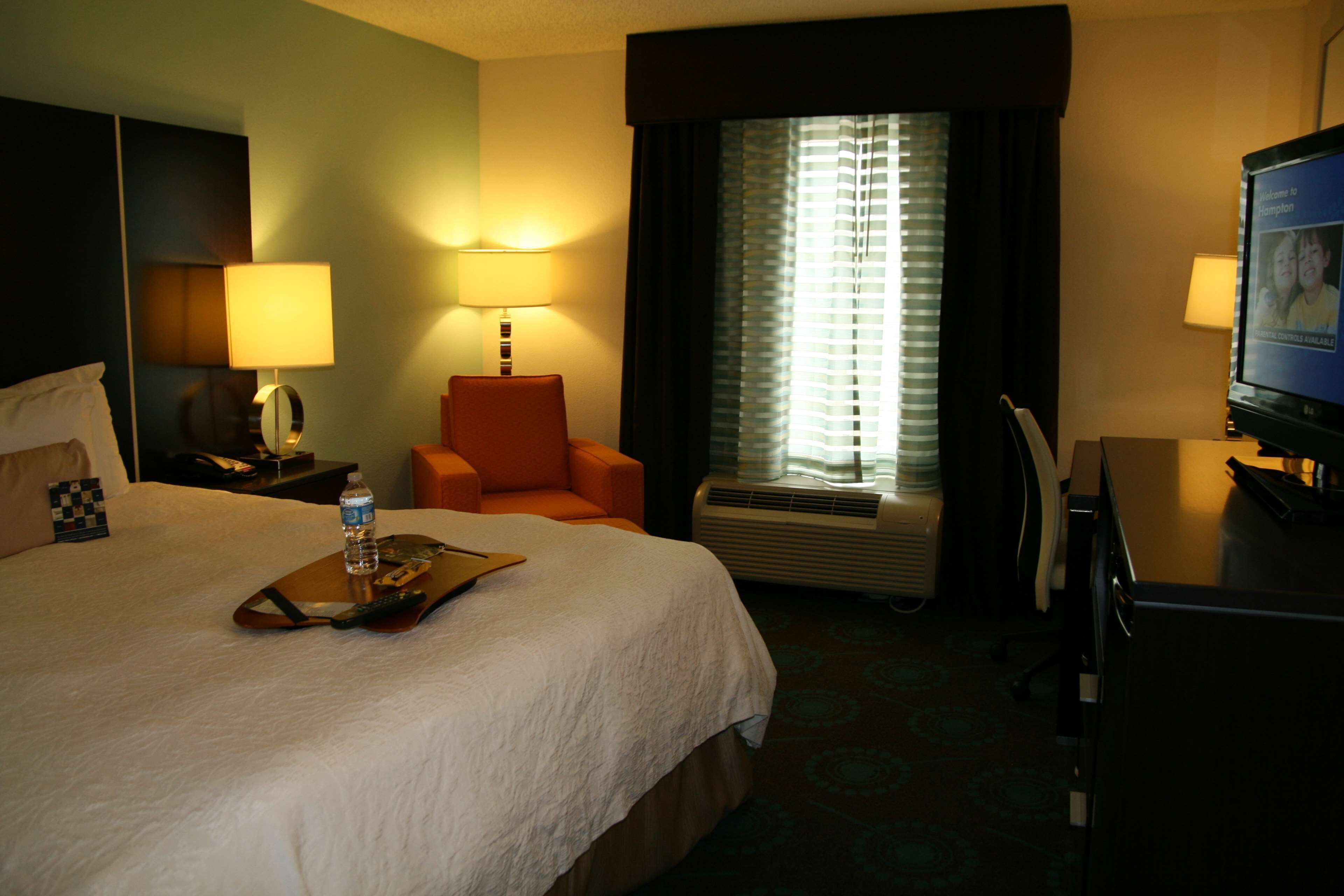 Een hotelkamer met een groot bed, twee bedlampen, een stoel, een bureau met een computer en een televisie.