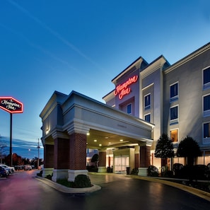 Un hôtel Hampton Inn avec une entrée bien visible, un panneau indiquant une hauteur libre de 12 pieds et un parking avec des voitures.