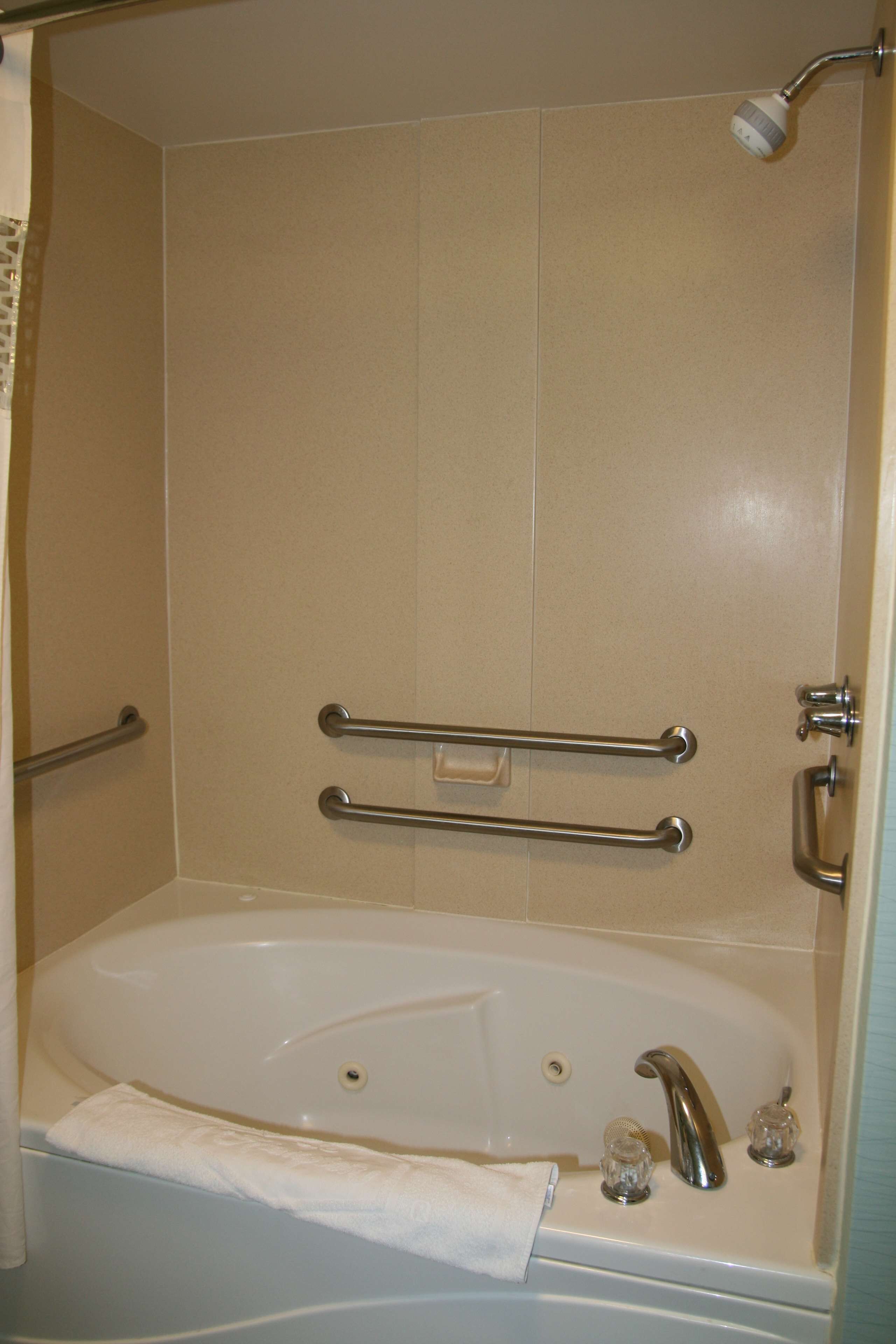 A bathtub with a showerhead, grab bars, and a towel.