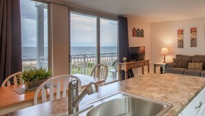 A modern living room with a kitchen area, a balcony with a view of the sea, and a staircase. - Villas By the Sea Resort & Conference Center (Jekyll Island)