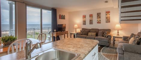 Una sala de estar moderna con área de cocina, un balcón con vistas al mar y una escalera.