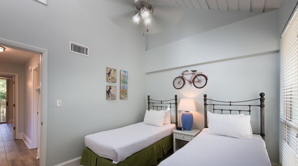 A bedroom with two single beds, a ceiling fan, a wall-mounted bicycle, and a small table with a lamp. - Villas By the Sea Resort & Conference Center (Jekyll Island)