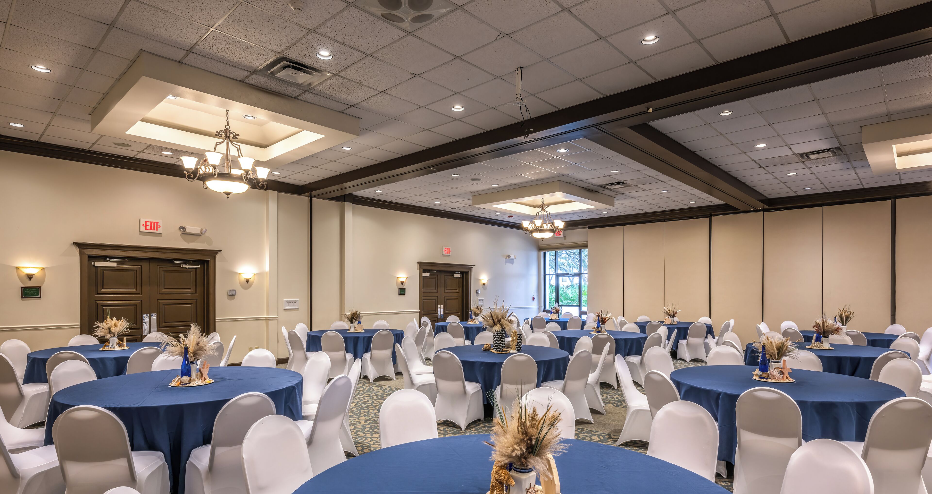 A conference room with multiple round tables, white chairs, and blue tablecloths.