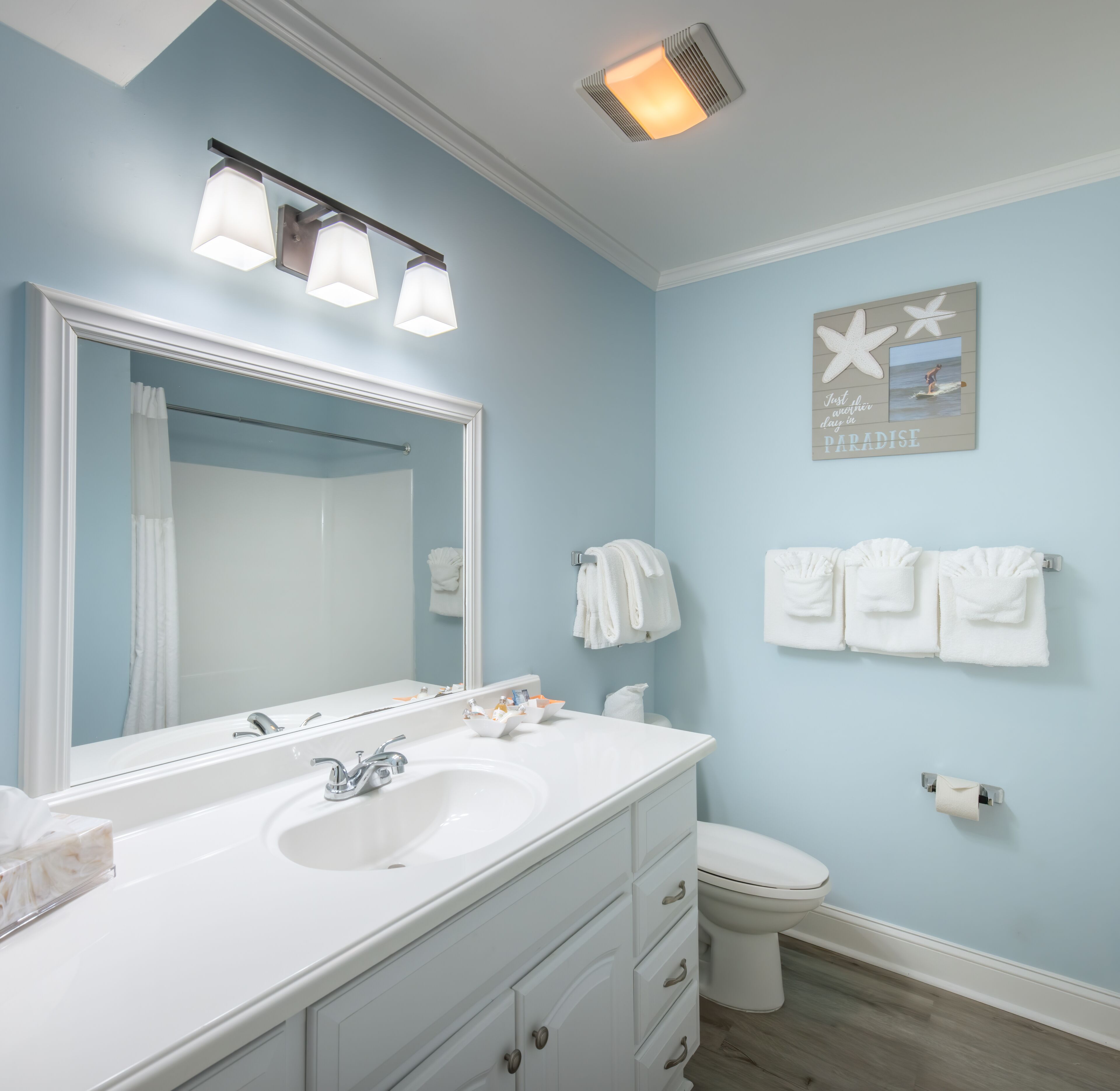 A bathroom with a white sink, mirror, and vanity, a toilet, and towels hanging on the wall.