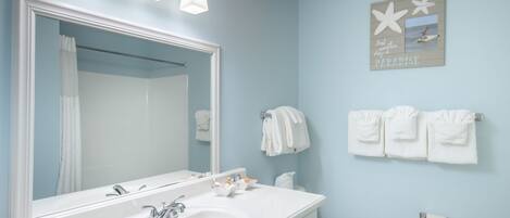 A bathroom with a white sink, mirror, and vanity, a toilet, and towels hanging on the wall.