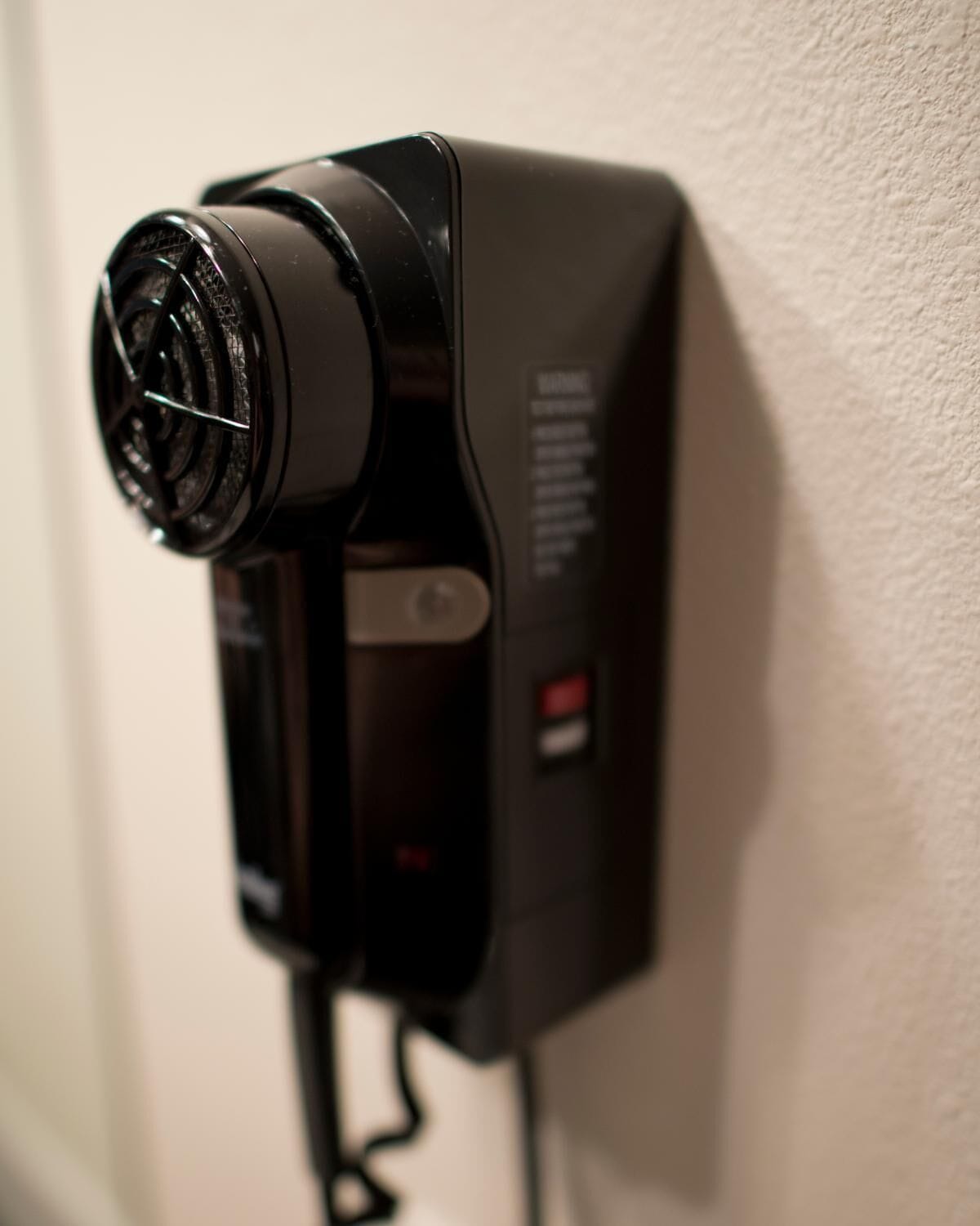 A black hair dryer mounted on a wall with a cord.