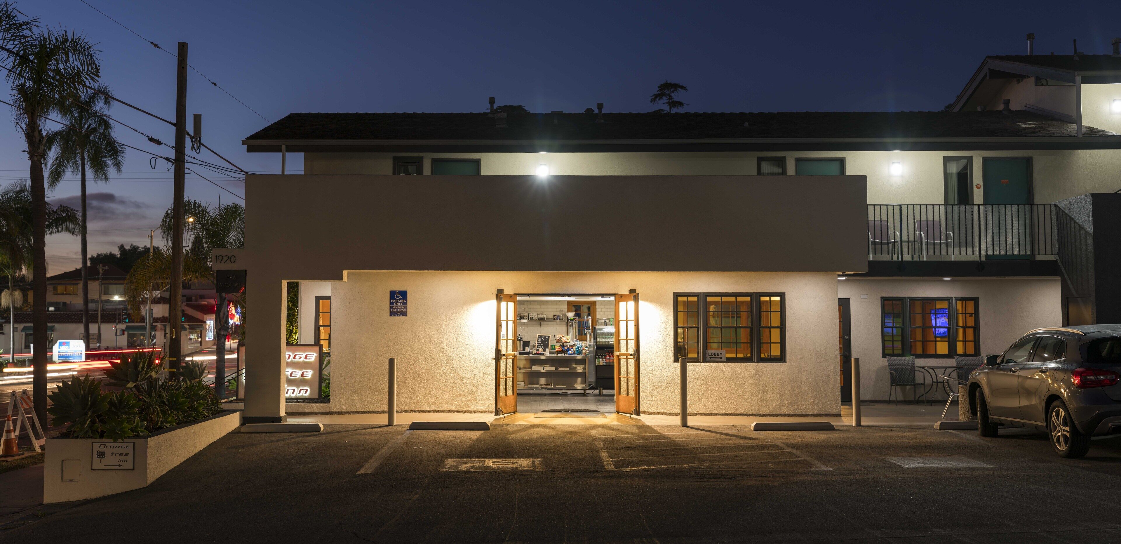 L’entrée d’un hôtel avec un parking, une enseigne bien visible indiquant « Orange Tree Inn », et une voiture garée à l’extérieur.