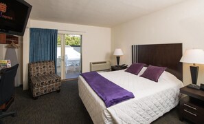 A hotel room with a bed, two bedside tables, a desk with a chair, a TV, and a sliding glass door to the outside. - Orange Tree Inn (Santa Barbara)